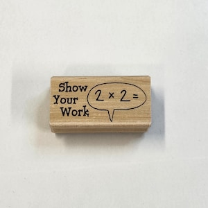 May include: A wooden stamp with the text "Show Your Work" and a speech bubble with the equation "2 x 2 =" inside.