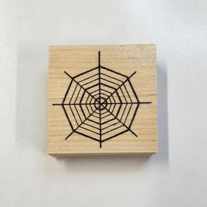 Könnte beinhalten: Ein Holzstempel mit einem schwarzen Spinnennetz-Design.