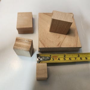 Peut inclure: Ensemble de blocs de bois non finis et une planche rectangulaire. Un mètre ruban jaune indique la taille d'un des blocs. Les blocs sont de tailles et formes variées, avec le grain naturel du bois.