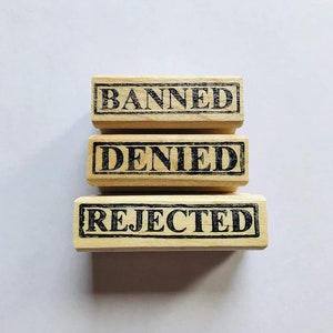 May include: Three wooden stamps with the words "Banned", "Denied", and "Rejected" printed in black ink.