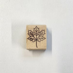 May include: A wooden stamp with a black outline of a maple leaf.