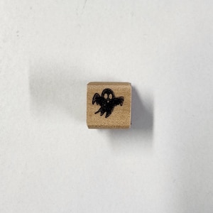 Op de afbeelding: Een houten stempel met een zwart silhouet van een geest met twee ogen.