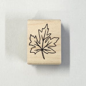 May include: A wooden stamp with a black line drawing of a maple leaf.