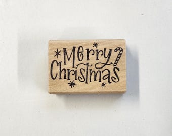 以下が含まれることがあります： 「*メリークリスマス*」の文字とキャンディーケーンのグラフィックが描かれた木製ゴム印です。