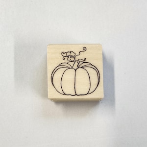 Peut inclure: Un tampon en bois avec un dessin au trait d'une citrouille avec une tige et des feuilles.