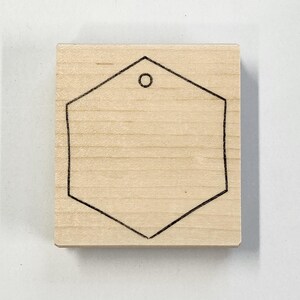 Op de afbeelding: Een blanco houten zeshoekige tag met een gat bovenaan om op te hangen.