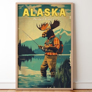 Op de afbeelding: Ingelijste kunstdruk met een elandachtig figuur dat in een meer vist. Het kunstwerk heeft een vintage reisposterstijl, met het woord "ALASKA" in gele blokletters bovenaan. De eland draagt een geruit overhemd en waadpak.