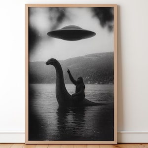 May include: Black and white framed print featuring a lake scene with a creature resembling the Loch Ness Monster, ridden by a figure pointing upwards at a hovering UFO. The artwork has a vintage, grainy aesthetic.