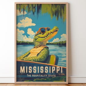 Op de afbeelding: Een ingelijste vintage poster met een alligator met een zonnebril en een geel shirt, in een boot op een meer. De poster leest "MISSISSIPPI" en "THE HOSPITALITY STATE", met een blauwe lucht en wolken.