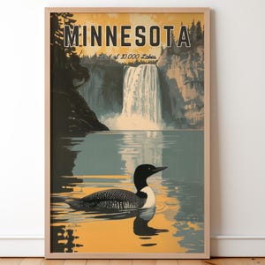 Op de afbeelding: Ingelijste kunstdruk met een schilderachtige illustratie van Minnesota. Het kunstwerk toont een waterval, een meer en een ijsvogel. Het woord "MINNESOTA" staat bovenaan, met "Land of 10,000 Lakes" eronder. Het kleurenpalet bevat tinten blauw, geel en bruin.