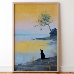 Op de afbeelding: Een ingelijst landschapsschilderij toont een serene waterkant. Een zwarte kat zit op de oever en kijkt naar het water. De lucht gaat over van geel naar blauw, met een klein huis en een boom aan de horizon. Het schilderij zit in een licht houten frame.