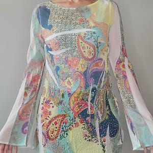 May include: A sheer, long-sleeved blouse with a colourful paisley print and beaded embellishments. The blouse has a scoop neck and bell sleeves.
