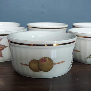 Puede incluir: Juego de seis ramequines de cerámica blanca con ribete dorado y diseños florales. Cada ramequín presenta un diseño diferente con bayas y hojas.