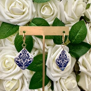 May include: A pair of blue and white ceramic earrings with a gold-tone hook closure. The earrings feature a damask pattern.