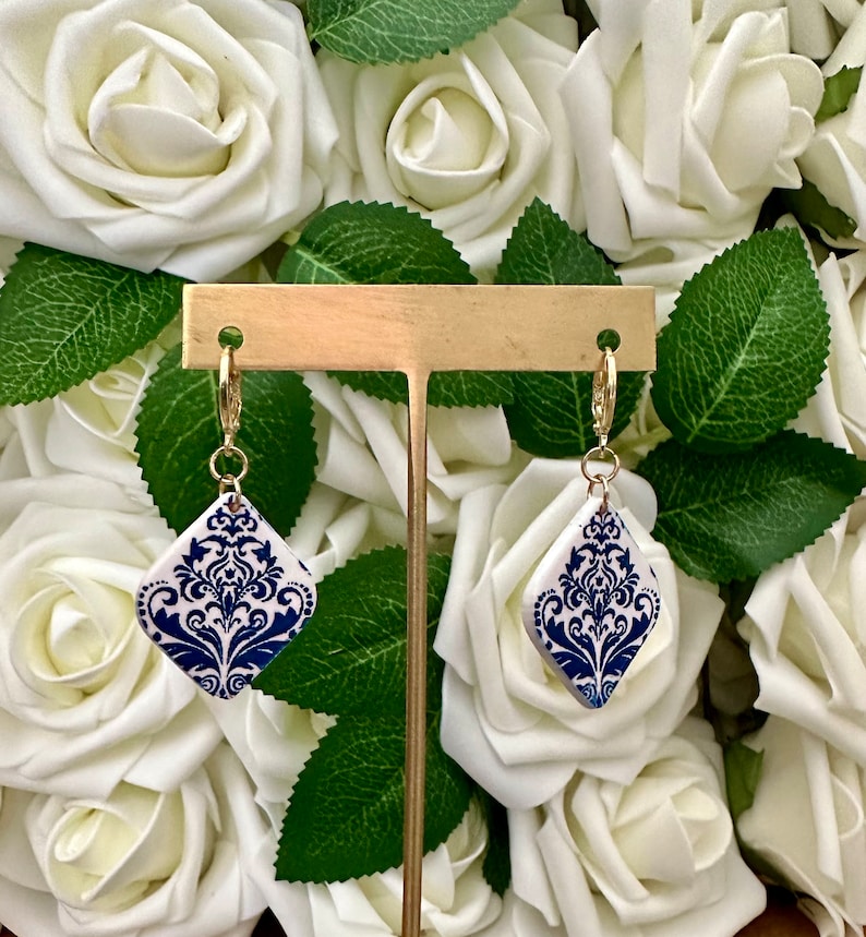 May include: A pair of blue and white ceramic earrings with a gold-tone hook closure. The earrings feature a damask pattern.