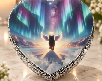 May include: A heart-shaped keepsake box with a silver-toned metal border featuring intricate embossed scrollwork. The lid displays a colorful illustration of a black cat with white wings and a halo, walking toward a bright light under an aurora.