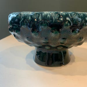 May include: A green ceramic bowl with a textured surface and a white swirl design. The bowl is on a pedestal.