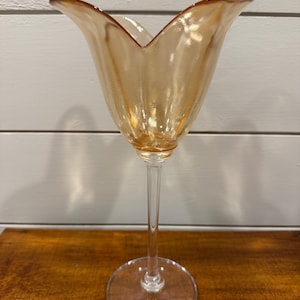 Pode incluir: Um copo alto, âmbar, com uma taça em forma de tulipa e uma haste fina. O copo tem uma base larga e transparente. O copo é provavelmente usado para servir bebidas. O copo está sobre um fundo neutro.