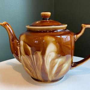 May include: A brown ceramic teapot with a white swirl design. The teapot has a lid and a handle.