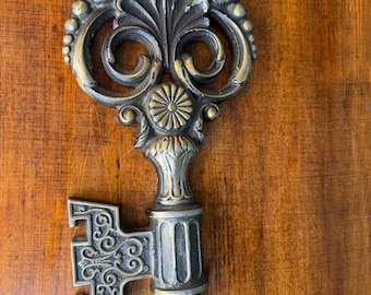 May include: Ornate, antique-style key with a decorative design. The key features a detailed head with floral and scrollwork elements, and a textured, aged finish. The key's handle and bit also have intricate patterns, suggesting a vintage or historical aesthetic.