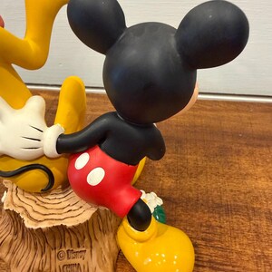 K&ouml;nnte beinhalten: Eine Keramikfigur von Mickey Mouse in seiner klassischen Kleidung, mit schwarzen Ohren, roten Shorts mit wei&szlig;en Kn&ouml;pfen und gelben Schuhen. Die Figur posiert mit Pluto, und die Basis ist ein Baumstumpf. Die Figur ist mit "&copy; Disney CHINA" gekennzeichnet.