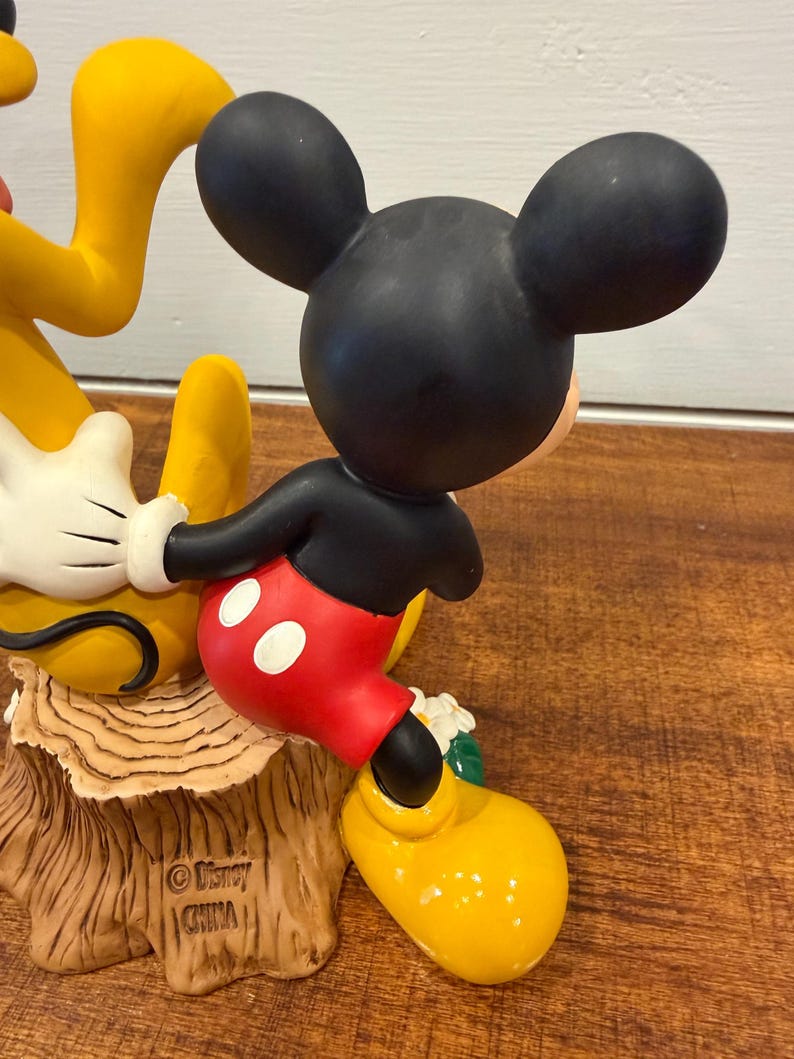 K&ouml;nnte beinhalten: Eine Keramikfigur von Mickey Mouse in seiner klassischen Kleidung, mit schwarzen Ohren, roten Shorts mit wei&szlig;en Kn&ouml;pfen und gelben Schuhen. Die Figur posiert mit Pluto, und die Basis ist ein Baumstumpf. Die Figur ist mit "&copy; Disney CHINA" gekennzeichnet.