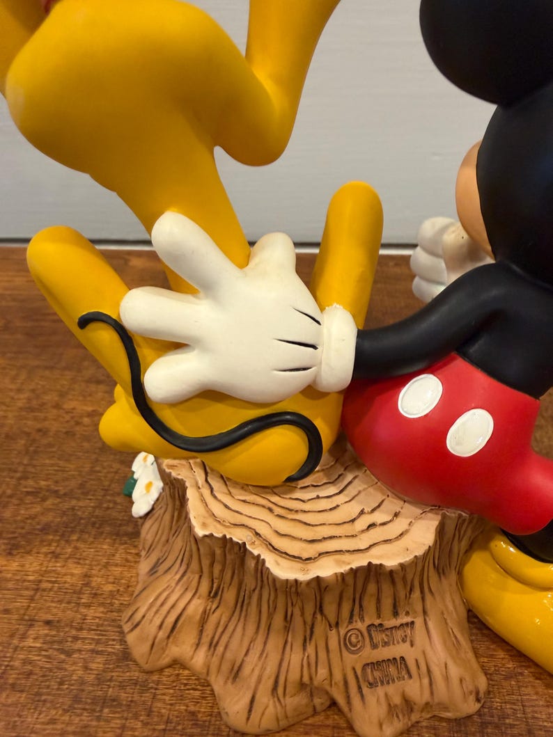 K&ouml;nnte beinhalten: Eine Disney-Figur mit Mickey Mouse in roten Shorts und schwarzen Handschuhen und Pluto in Gelb. Der Sockel ist ein Baumstumpf mit den Disney- und China-Marken.