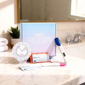 Op de afbeelding: Een verzameling zwangerschapstests en gerelateerde items, waaronder een doos met de tekst "100% CERTAIN", een cirkelvormig wiel en verschillende teststicks. De tests zijn in verschillende vormen, met roze en blauwe accenten.