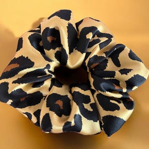 Può includere: Un elastico per capelli in raso con stampa leopardata oro e nero.