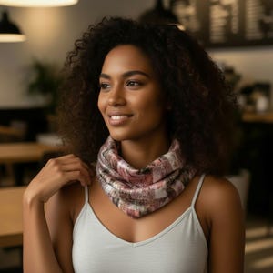 Può includere: Una sciarpa a quadri rosa, bianca e marrone è indossata intorno al collo. La sciarpa è realizzata in un materiale morbido e presenta un motivo quadrato. La persona nell'immagine indossa una canotta grigio chiaro.