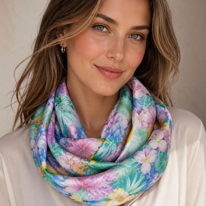 Könnte beinhalten: Ein Schal mit floralem Muster. Das Design zeigt rosa, blaue und gelbe Blumen auf einem hellblauen und grünen Hintergrund. Der Schal ist aus weichem, seidigem Material gefertigt.