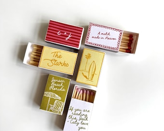 Peut inclure: Cinq boîtes d'allumettes rectangulaires avec divers motifs et textes. L'une présente des rayures rouges et 'C + J', d'autres portent les inscriptions 'A match made in Heaven', 'The Starks', 'Jensen Beach, Florida' avec une chaise de plage, et 'If you are reading this, Jack + Caty love you'.