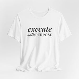 Może przedstawiać: Biała koszulka z czarnym napisem "execute with PURPOSE".
