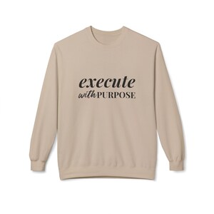 May include: A beige long-sleeved sweatshirt with the text "execute with PURPOSE" printed in black on the front.