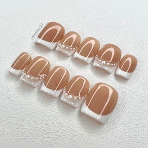 May include: Set of ten nude-colored press-on nails with white tips and pearl accents.