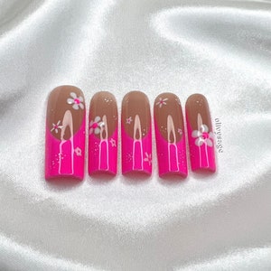 May include: Six pink and brown fake nails with white flower designs.