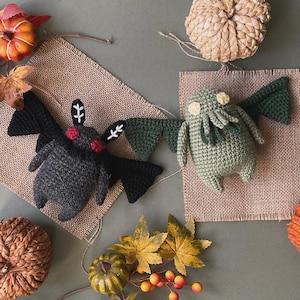May include: Two crocheted plush toys, a black bat and a green Cthulhu, on a hessian background. The bat has red eyes and white accents. The Cthulhu has yellow eyes and tentacles.