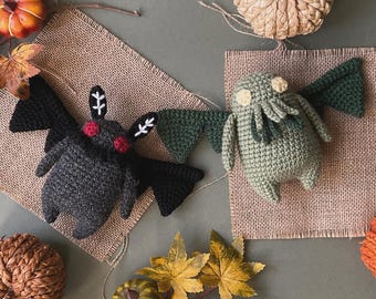 May include: Two crocheted plush toys, a black bat and a green Cthulhu, on a burlap background. The bat has red eyes and white accents. The Cthulhu has yellow eyes and tentacles.