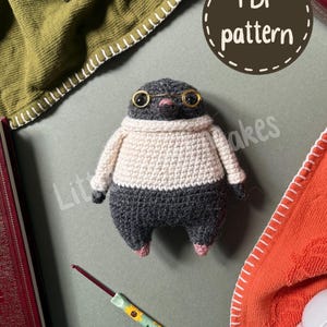 May include: A crocheted mole doll with dark gray fur, wearing a cream-colored sweater and small gold-rimmed glasses. The mole has a pink nose and small pink feet. A circular brown graphic with the text PDF pattern is visible above the doll.