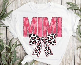 May include: White t-shirt with the word "MIMI" in pink glitter letters with a pink and black leopard print bow.