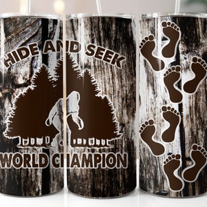 May include: Three stainless steel tumblers with a wood grain pattern. The center tumbler has the text "HIDE AND SEEK WORLD CHAMPION" and a silhouette of a person hiding behind trees. The tumbler on the right has footprints on it.