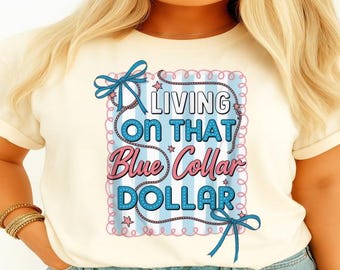 Può includere: T-shirt color crema con un design grafico. Il design presenta il testo "LIVING ON THAT Blue Collar DOLLAR" in blu e rosa, su uno sfondo a righe blu e bianche, con fiocchi decorativi.