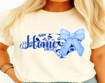 May include: A white t-shirt with a blue and white floral design of the state of North Carolina and the word "Home" in blue lettering. A blue bow is above the state.