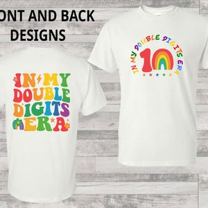 May include: White t-shirt with colorful text and graphics. The front design says "IN MY DOUBLE DIGITS ERA" with a rainbow and the number 10. The back has the same text in a retro font.