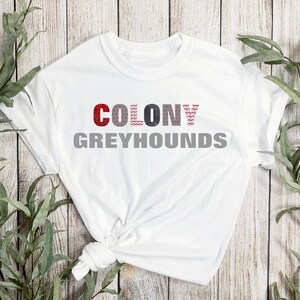May include: White t-shirt with the text "COLONY GREYHOUNDS" in red, black, and gray lettering.