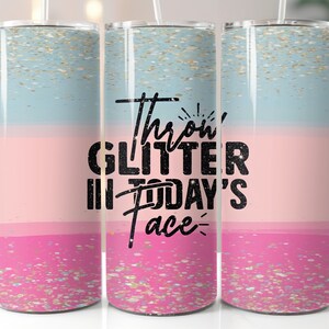 May include: Three stainless steel tumblers with a pink and blue ombre glitter design. The middle tumbler has the text "Throw glitter in today's face" in black.