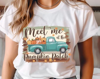 Può includere: Maglietta bianca con una grafica di un camioncino blu-verde pieno di zucche. Il testo "Meet me at the Pumpkin Patch" è stampato sulla maglietta.