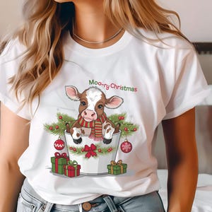 May include: White t-shirt with a brown and white cow wearing a red and green scarf sitting in a white bucket with Christmas ornaments and the text "Moo-ry Christmas".