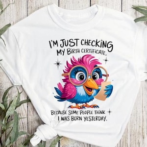 Könnte beinhalten: Weißes T-Shirt mit einem Cartoon-Vogel, der eine Brille trägt und ein Dokument hält. Der Text auf dem Shirt lautet "Ich überprüfe nur meinen Geburtsurkunde, weil manche Leute denken, dass ich gestern geboren wurde."