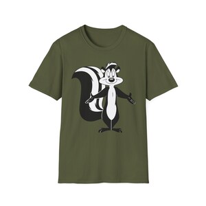 Pode incluir: T-shirt verde-oliva com um personagem de desenho animado de doninha em preto e branco. A doninha está com os braços abertos. A t-shirt é de gola redonda.